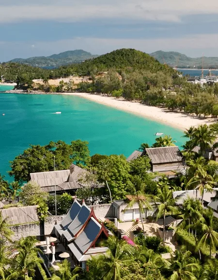 A sweeping high-angle view of Pansea Beach in Phuket, Thailand, Asia, featuring luxury villa rooftops with traditional Thai architecture nestled in lush palm trees overlooking a white sand crescent and turquoise ocean.